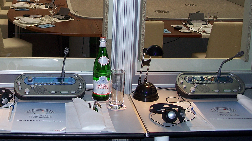 Description: A view through an interpreting booth shows two interpreters’ workplace in the foreground and a prepared executive dinner in the background.